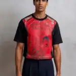 A man with short dark hair stands against a light gray wall, wearing the OVA CHEEVA Men’s Heavy Cotton Michael Jackson Beat It Graphic T-Shirt, which features text and an illustrated portrait on the front.