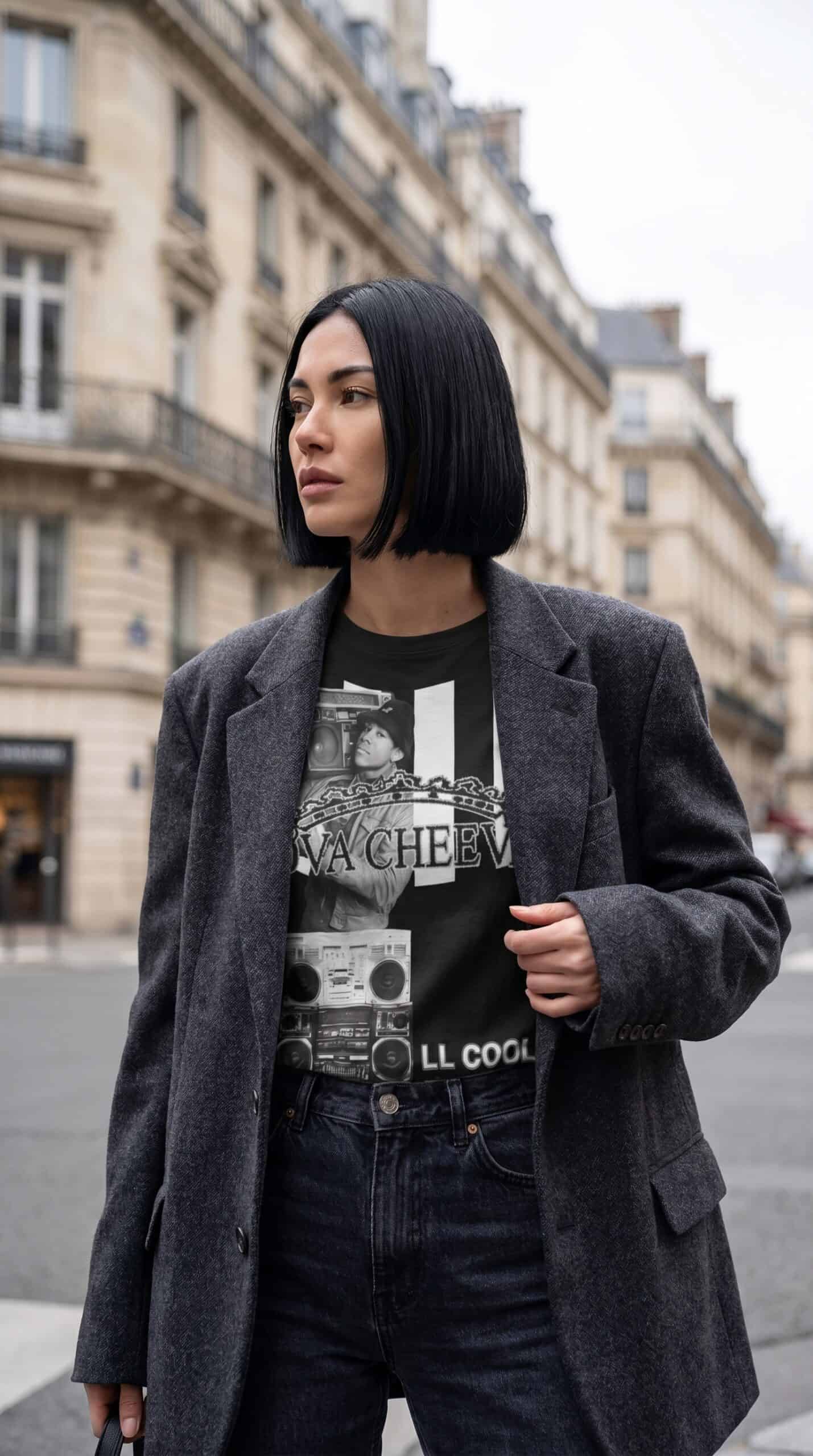 A woman with a sleek bob haircut wearing a graphic t-shirt and a dark blazer, standing on a city str.