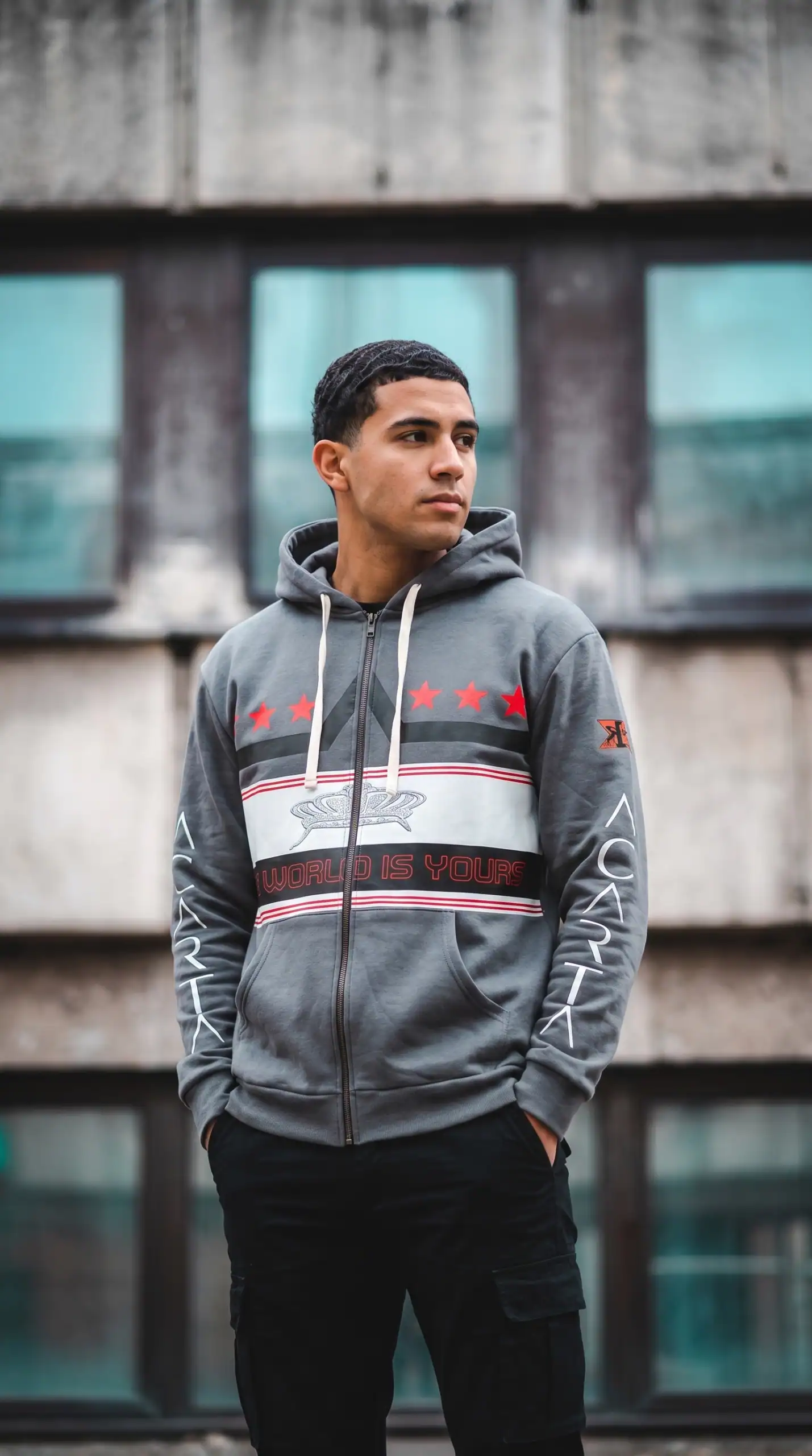 Young man in urban hoodie standing outdoors in front of a modern building.