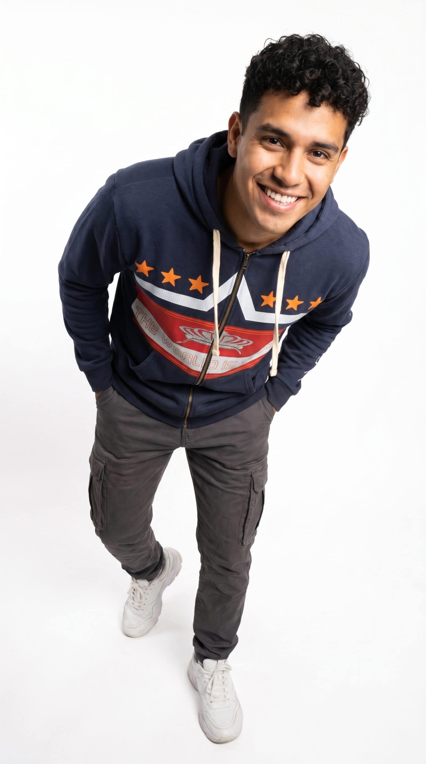 A young man smiling in a navy blue hoodie with red, white, and orange graphic design, standing again.