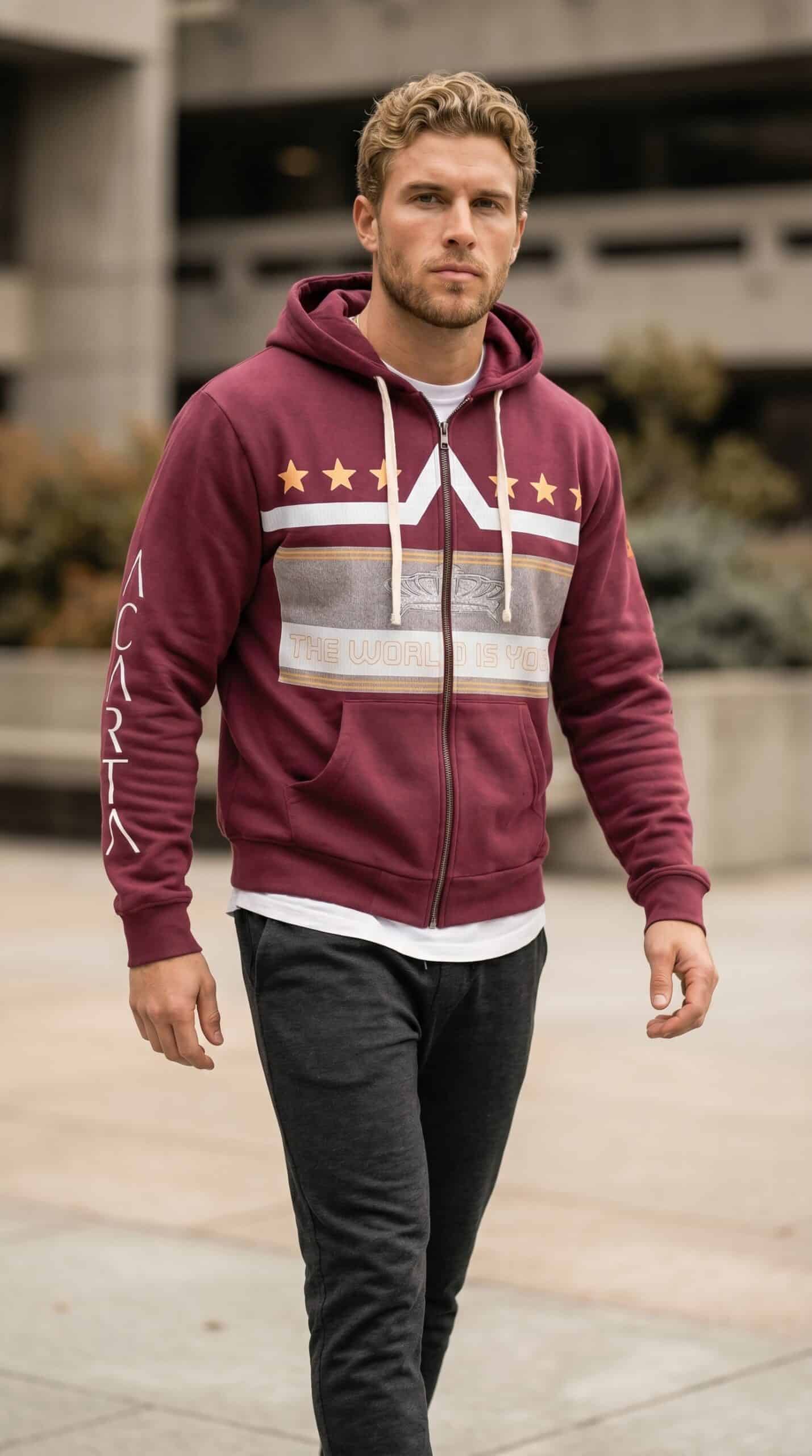 A stylish young man wearing a maroon zip-up hoodie with white and gold accents, standing outdoors.