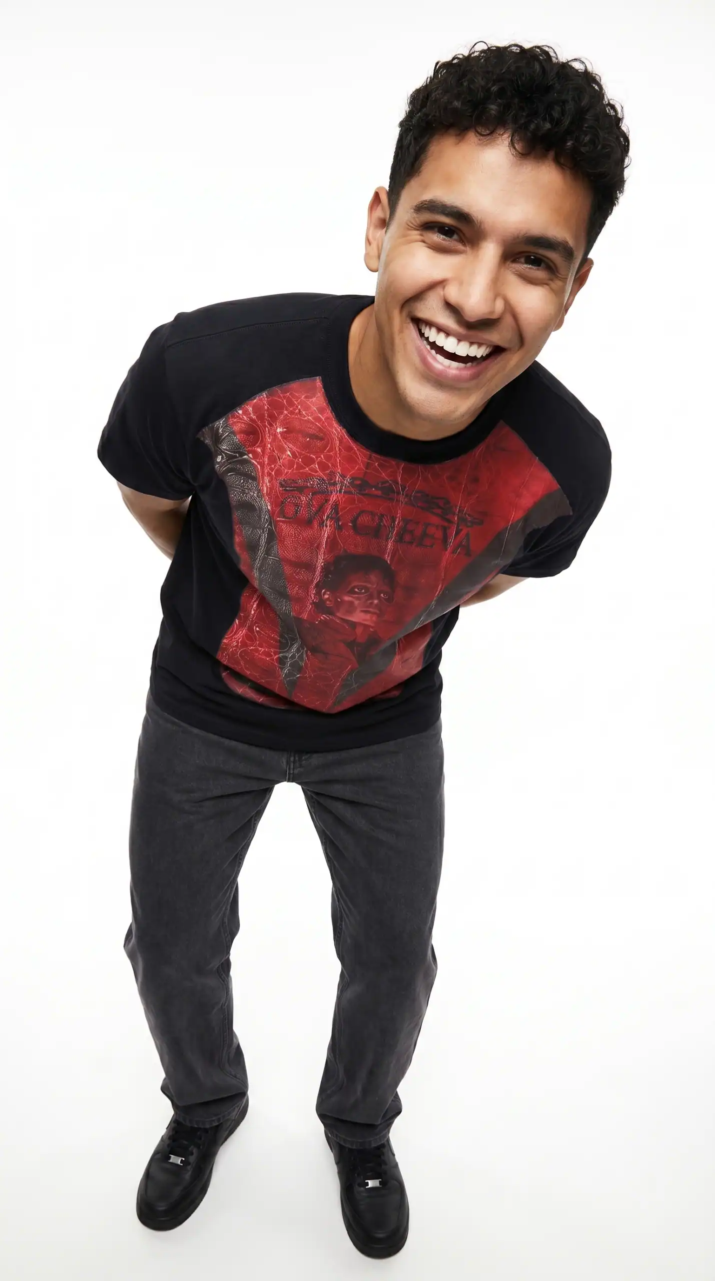 A young man smiling and leaning forward, wearing a graphic T-shirt and dark jeans.