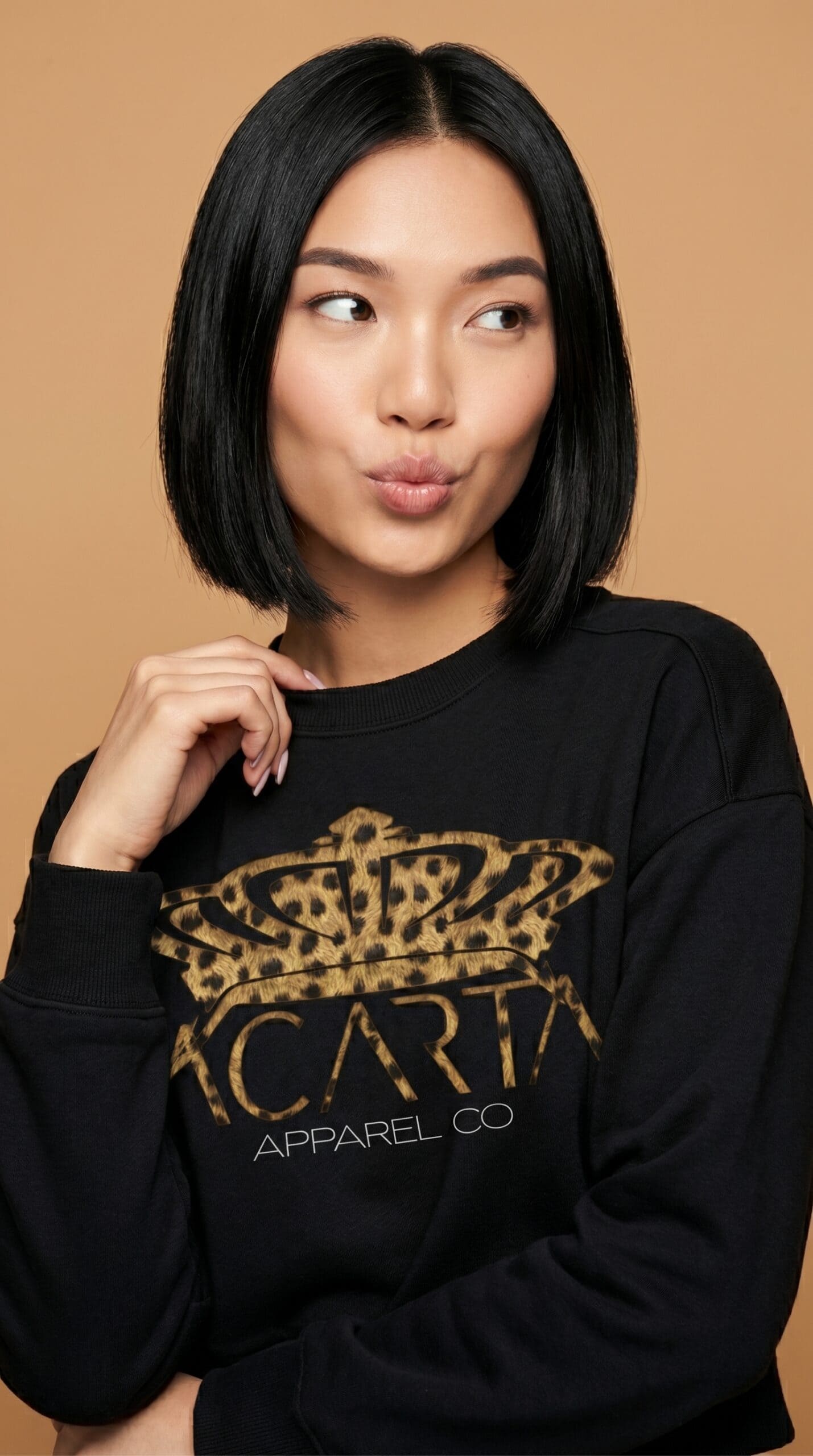 A woman with shoulder-length black hair wearing a black Too Dapper sweatshirt with a gold logo.