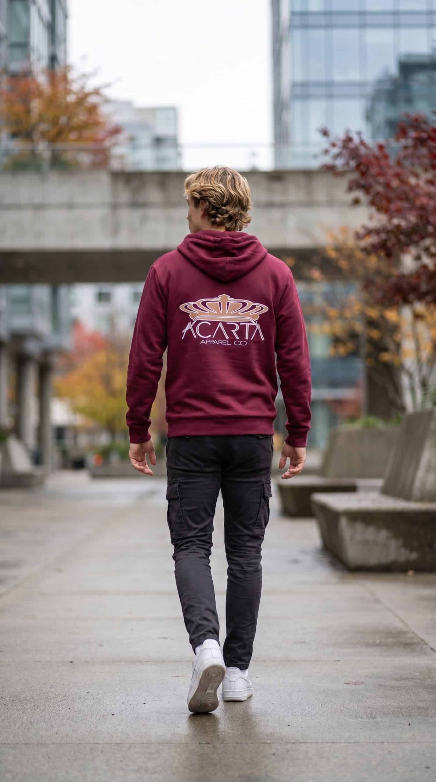 A man walking away in an urban setting wearing a maroon hoodie with "ACATA" logo.