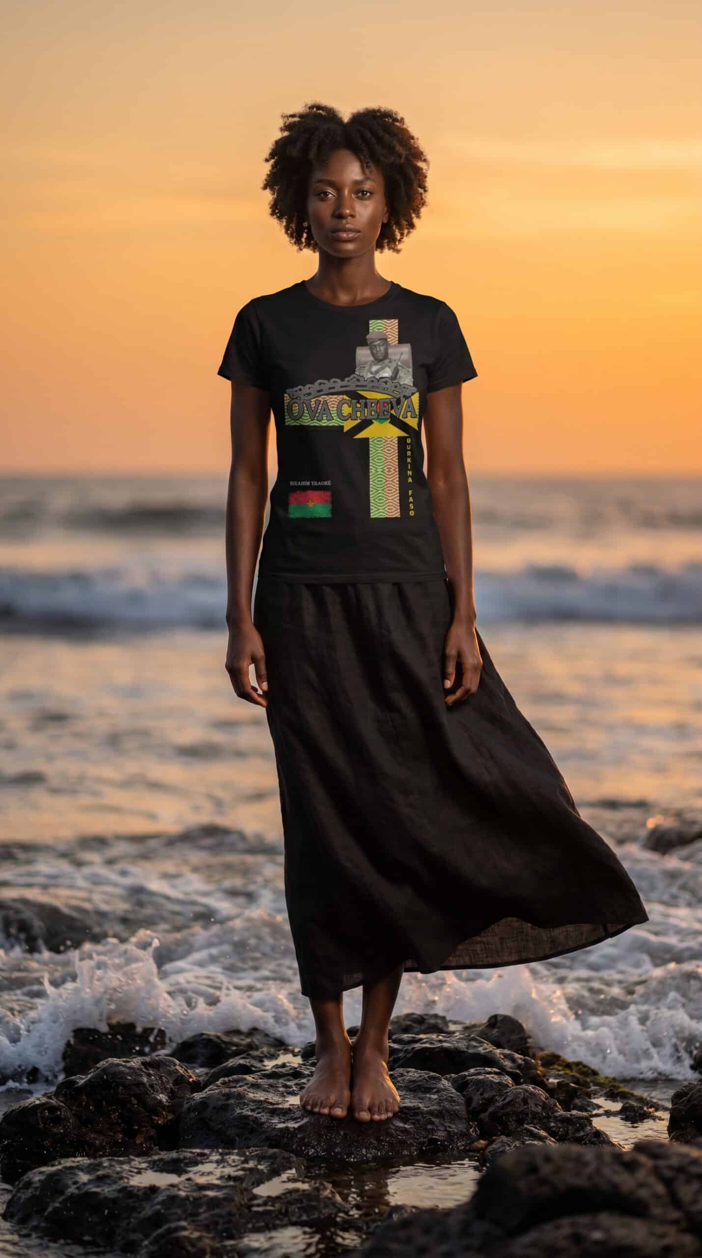 A woman standing barefoot on rocks at the beach during sunset, wearing a black graphic t-shirt and l.