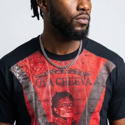 A man with dreadlocks wearing a graphic red and black T-shirt and silver chain necklace.
