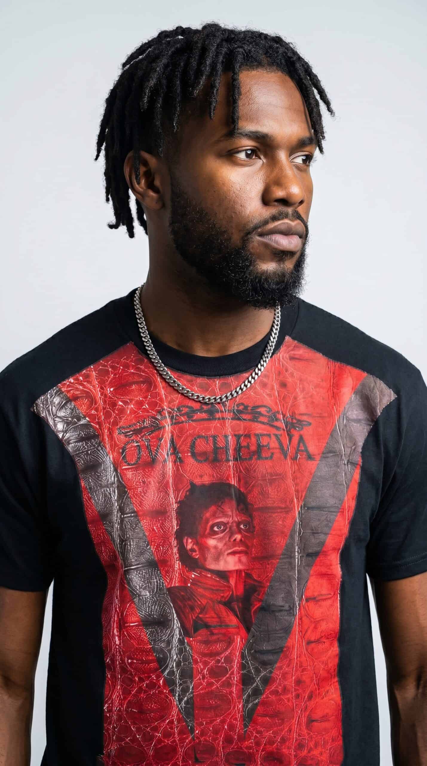A man with dreadlocks wearing a graphic red and black T-shirt and silver chain necklace.