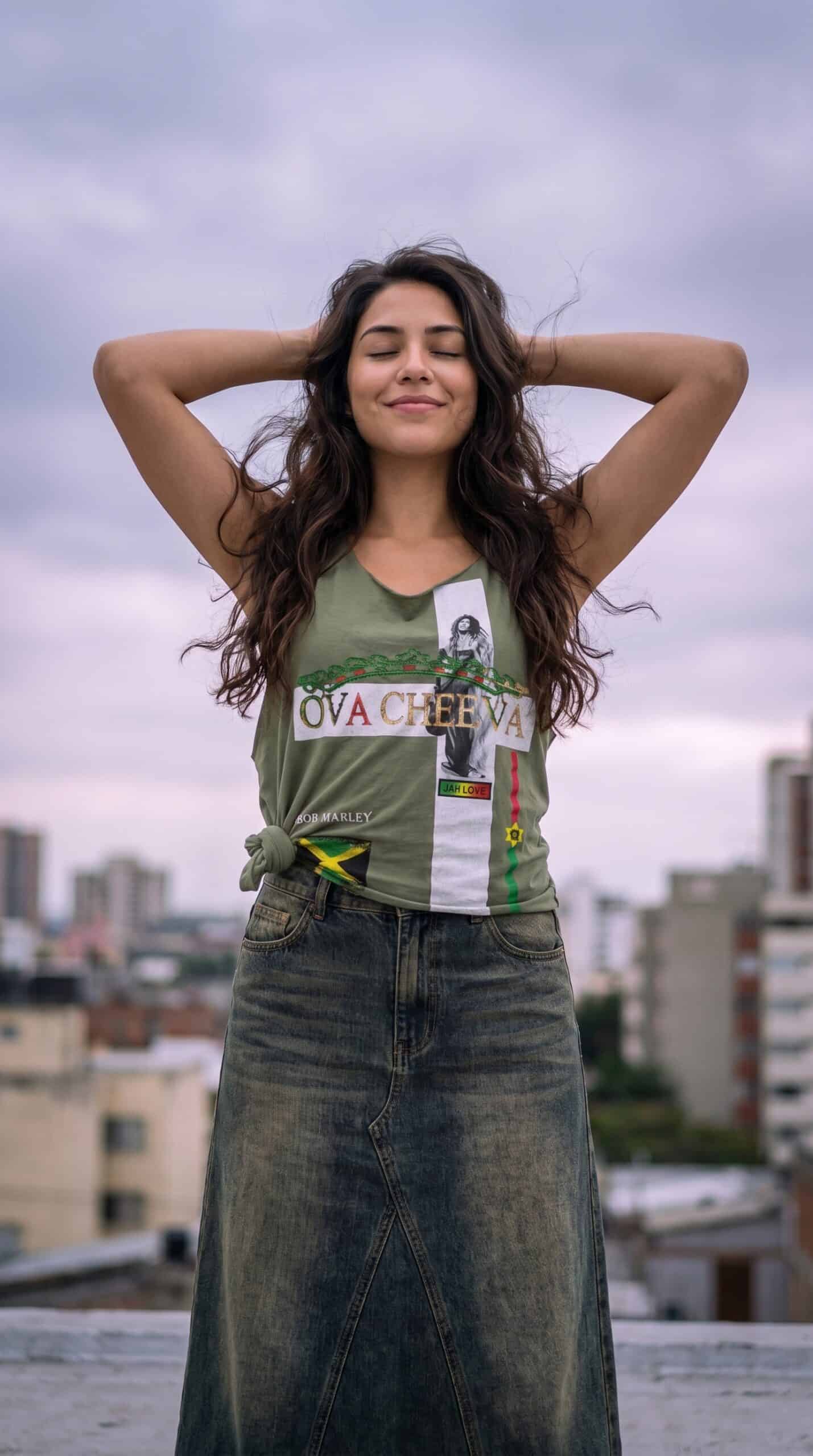A woman standing outdoors on a rooftop with a cityscape background, wearing casual urban apparel.