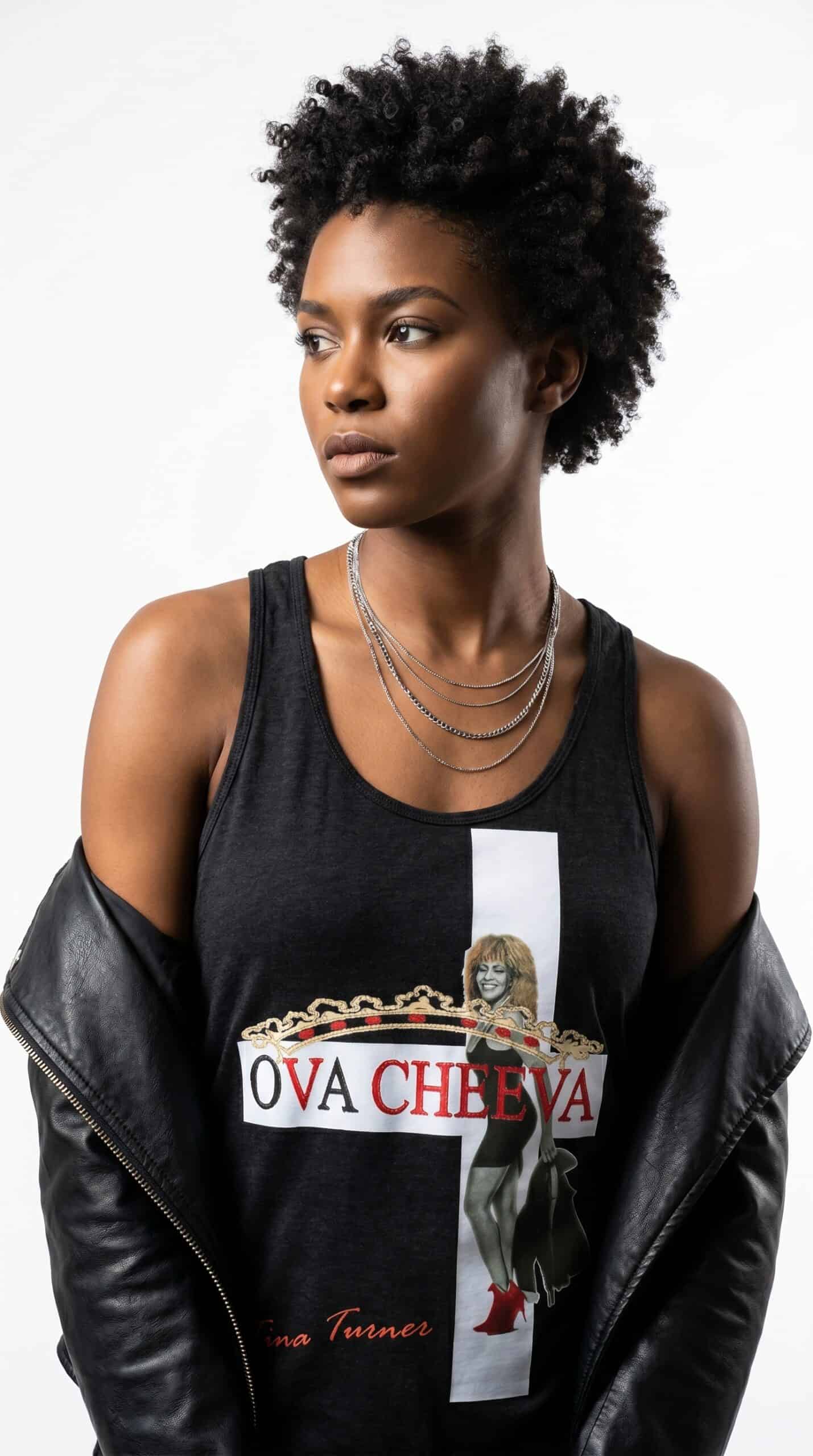 Bold woman with natural afro hairstyle wearing a graphic tank top and layered necklaces, showcasing.