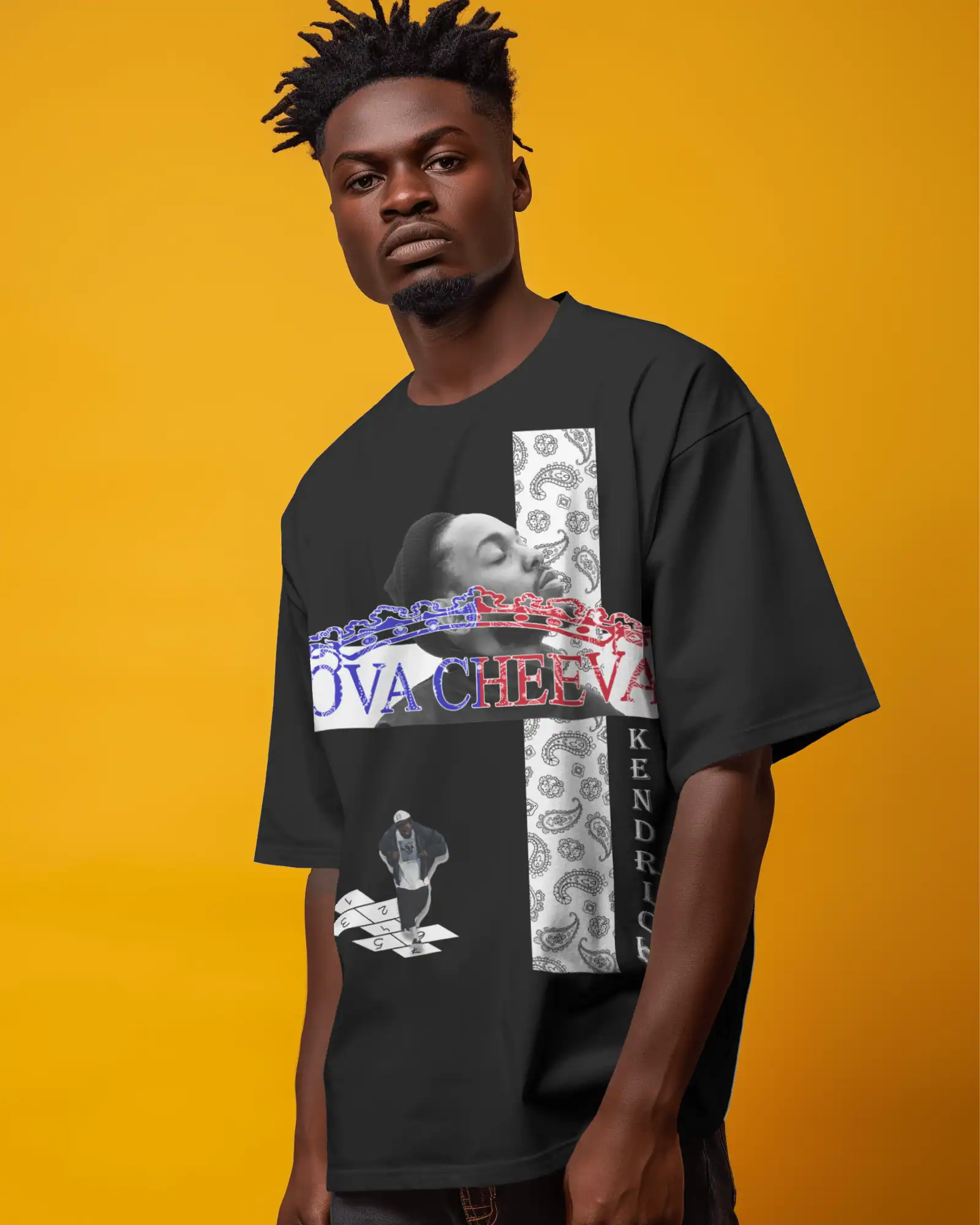 A man stands against a yellow background wearing a black t-shirt with bold graphic designs, including a grayscale portrait, red and blue text, and the word KENDRICK vertically printed on the side.