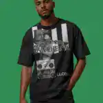 A man stands against a green background wearing a black graphic T-shirt featuring a boombox, a chain, and OVA CHEEVA text, along with “LL COOL J” at the bottom. He has short hair and a trimmed beard.