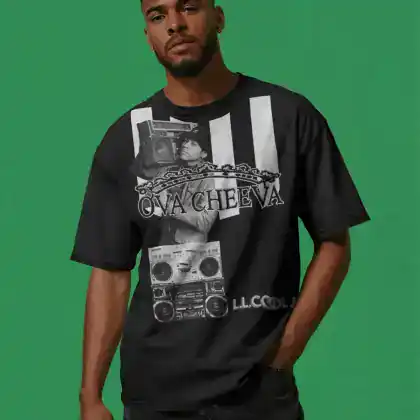 A man stands against a green background wearing a black graphic T-shirt featuring a boombox, a chain, and OVA CHEEVA text, along with “LL COOL J” at the bottom. He has short hair and a trimmed beard.