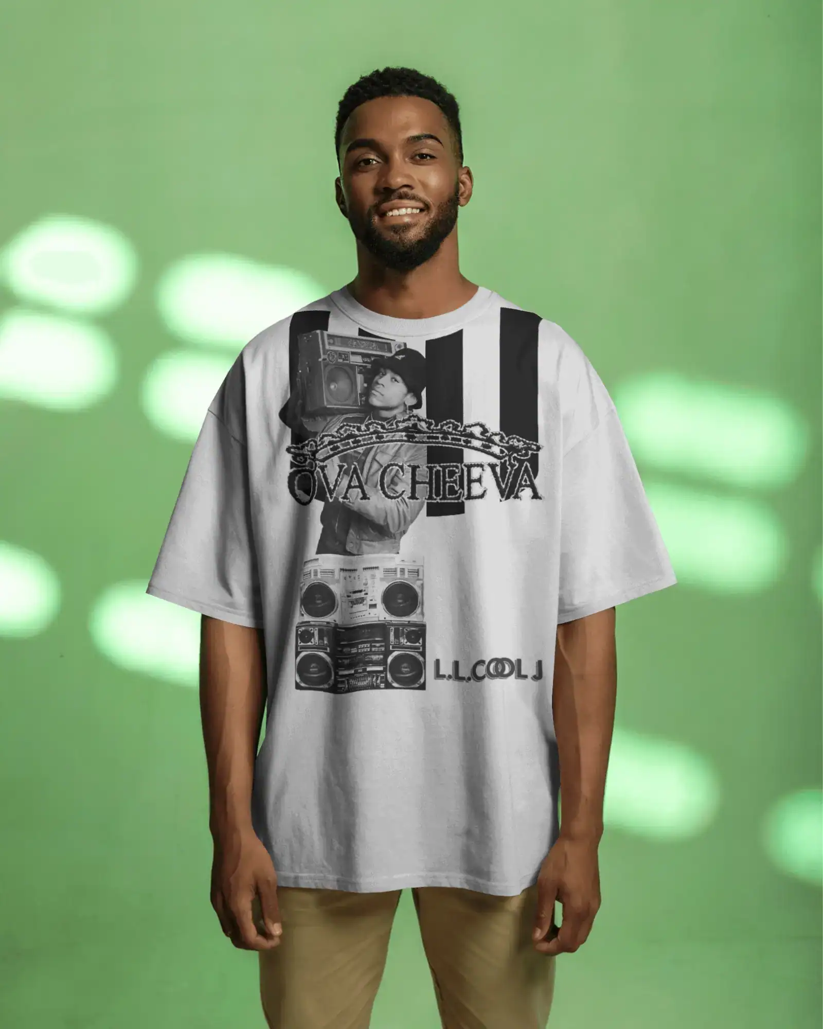 A man with a short beard smiles against a green background, wearing the OVA CHEEVA Men's Heavy Cotton L.L. Cool J. Graphic T-Shirt with black graphics and stylized text.