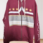 A maroon zip-up hoodie with cream drawstrings, gold stars, a gray and white graphic, and the phrase THE WORLD IS YOURS on the front. The sleeves have the word CARTA printed in white.
