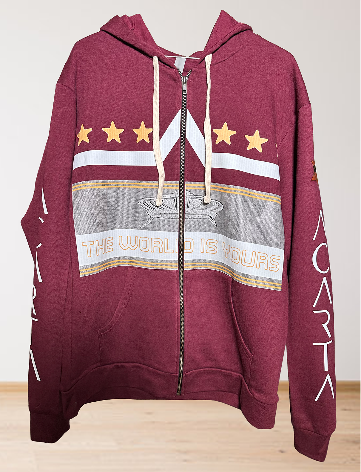 A maroon zip-up hoodie with cream drawstrings, gold stars, a gray and white graphic, and the phrase THE WORLD IS YOURS on the front. The sleeves have the word CARTA printed in white.