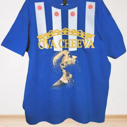 Blue t-shirt featuring vertical white stripes with red star designs, gold crown graphic, yellow text reading OVA CHEEVA, and an image of a tattooed person looking upward.