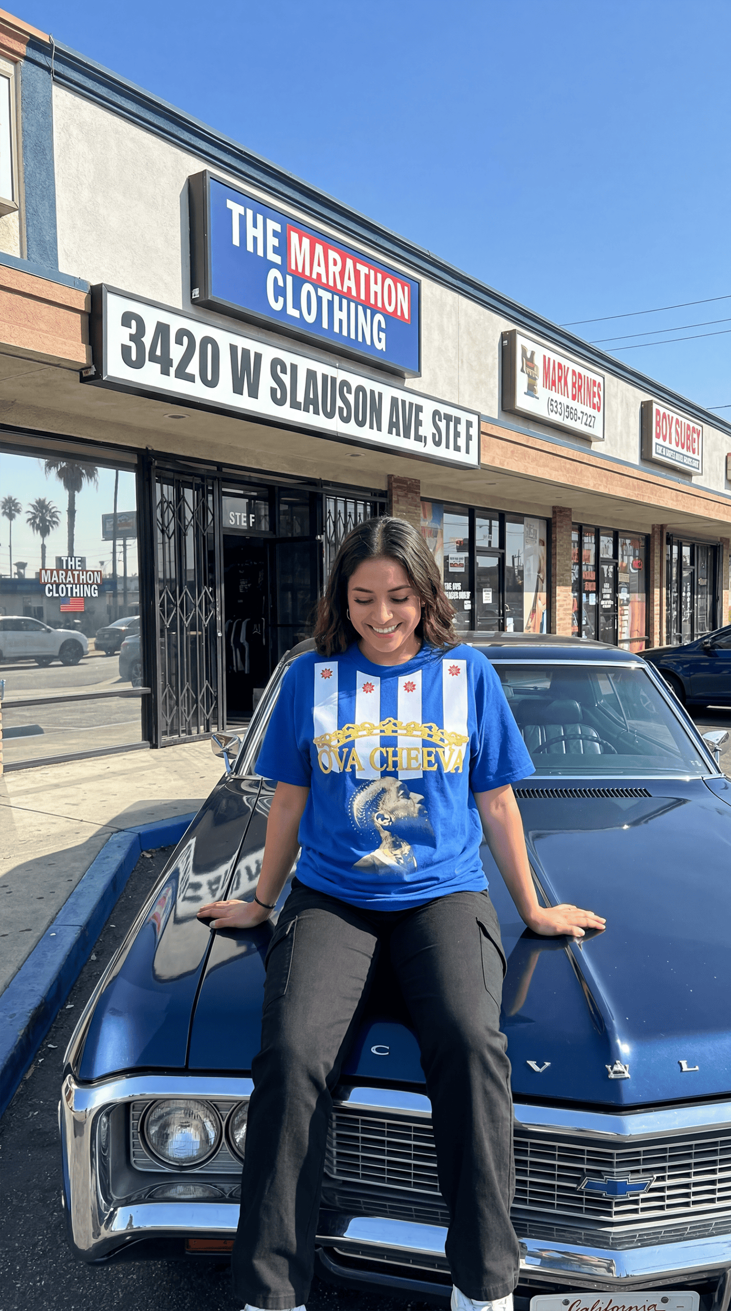 A woman sitting on the hood of a vintage Chevrolet outside a streetwear store.