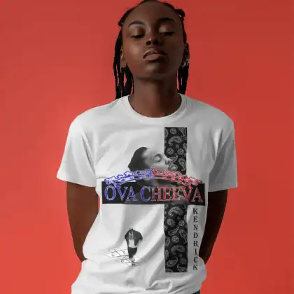 A person stands against a solid red background, hands behind their back, wearing the OVA CHEEVA Women’s Midweight Cotton Kendrick Lamar Graphic T-Shirt featuring bold designs, "OVA CHEEVA" and "KENDRICK," plus an artistic face illustration.