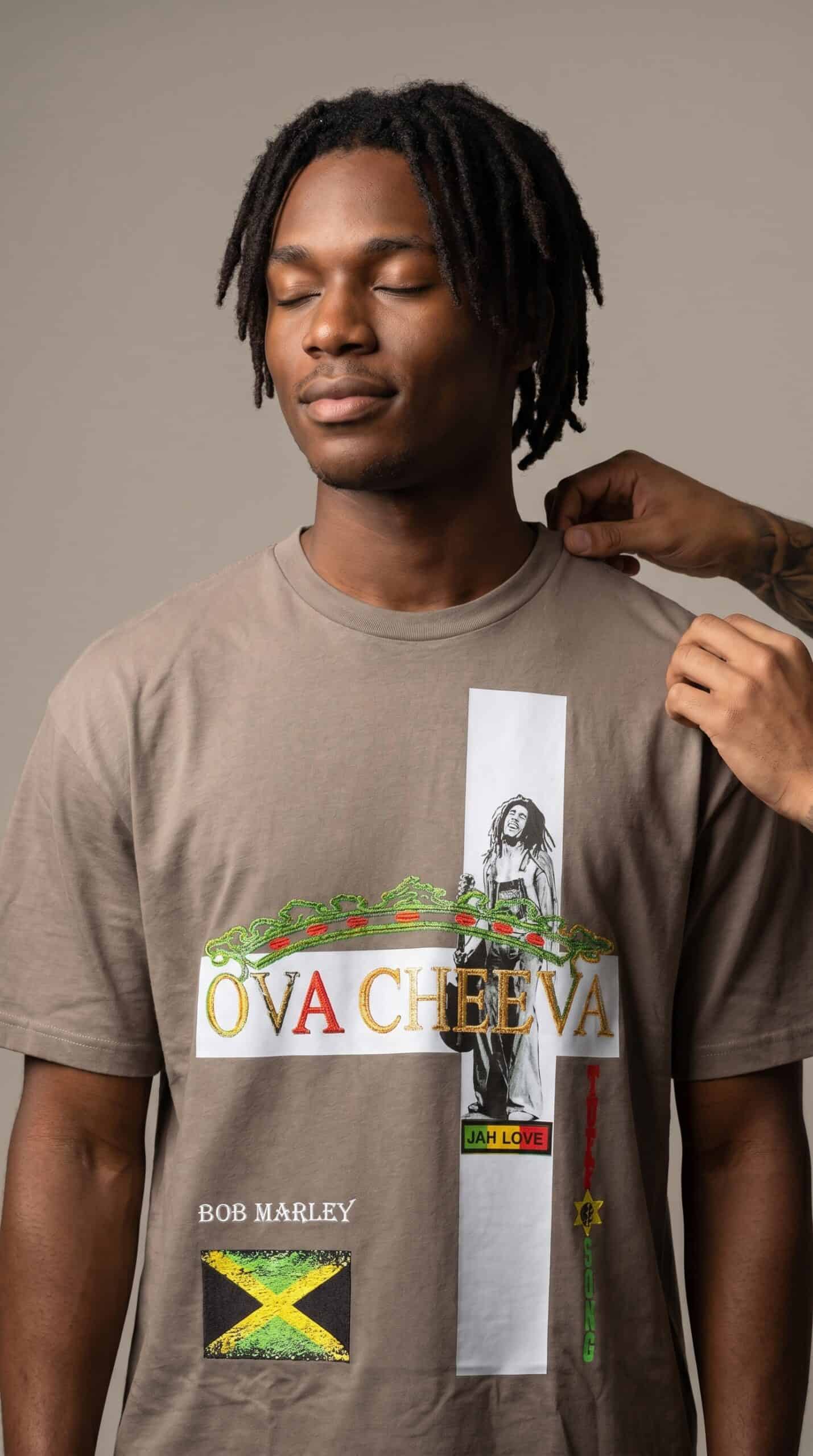 Stylish young man with dreadlocks wearing a graphic T-shirt celebrating urban culture and music.