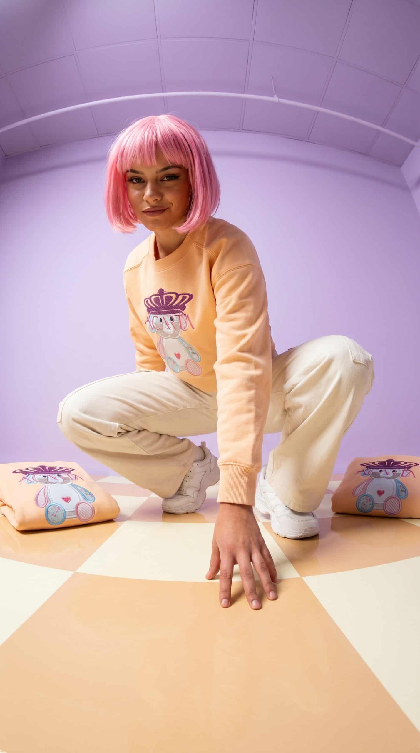 Bright pink-haired woman in casual urban apparel crouching on colorful floor with pillows, modern in.