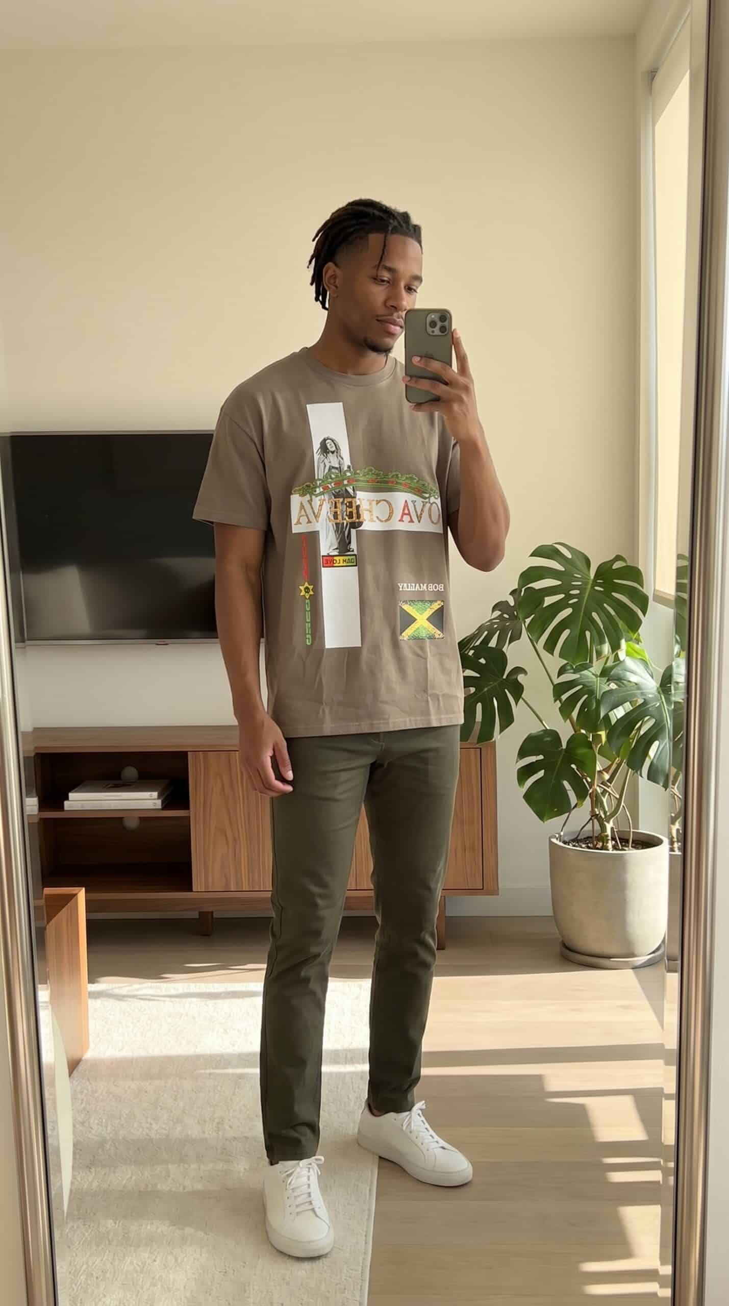 A young man taking a mirror selfie in a modern living room with a TV and a large potted plant.