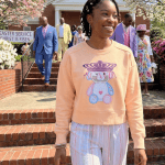 Young woman in apricot sweatshirt with bunny print, smiling outside church.