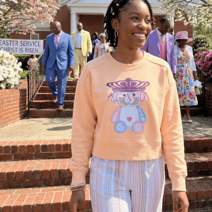 Young woman in apricot sweatshirt with bunny print, smiling outside church.