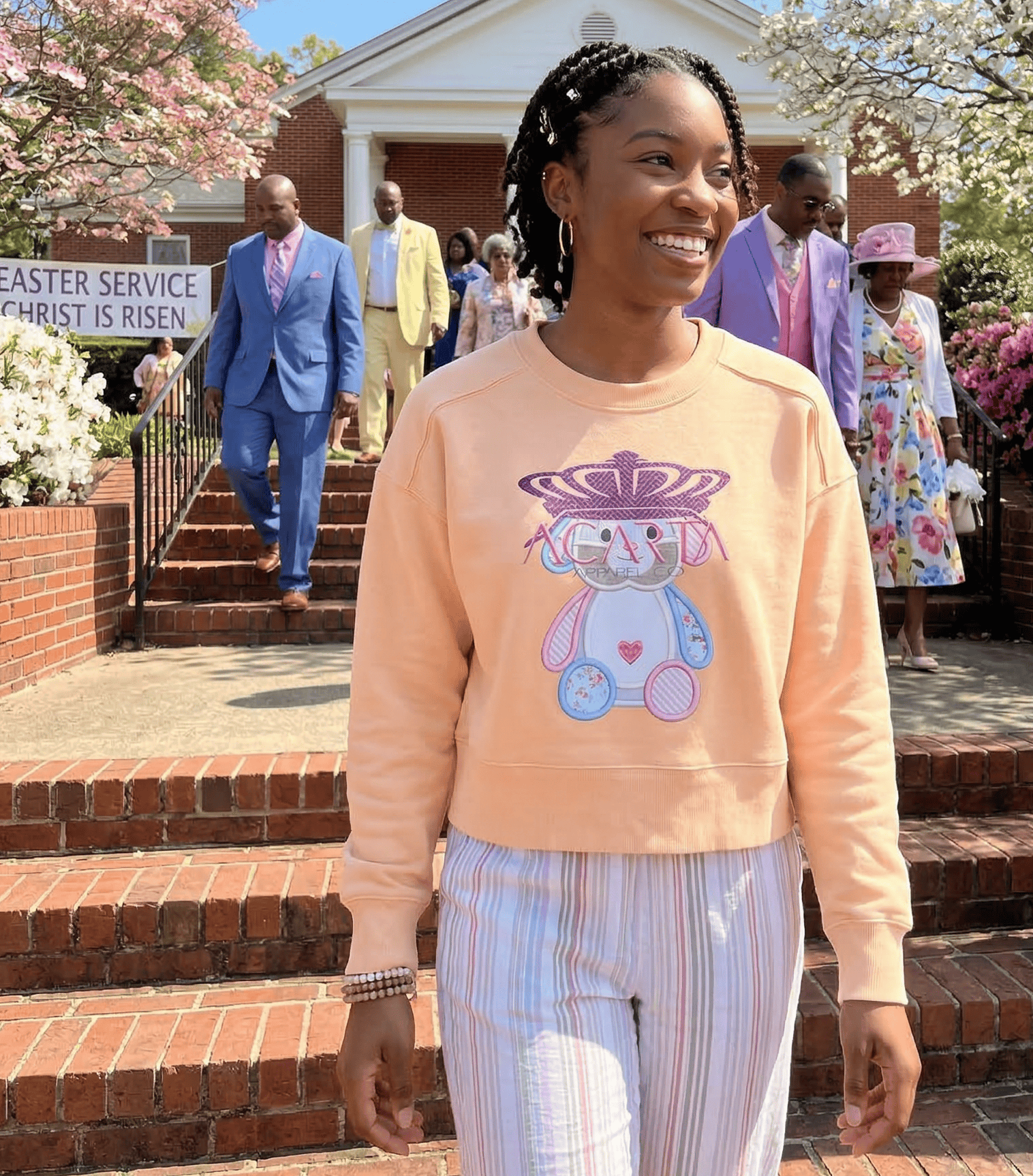 Young woman in apricot sweatshirt with bunny print, smiling outside church.