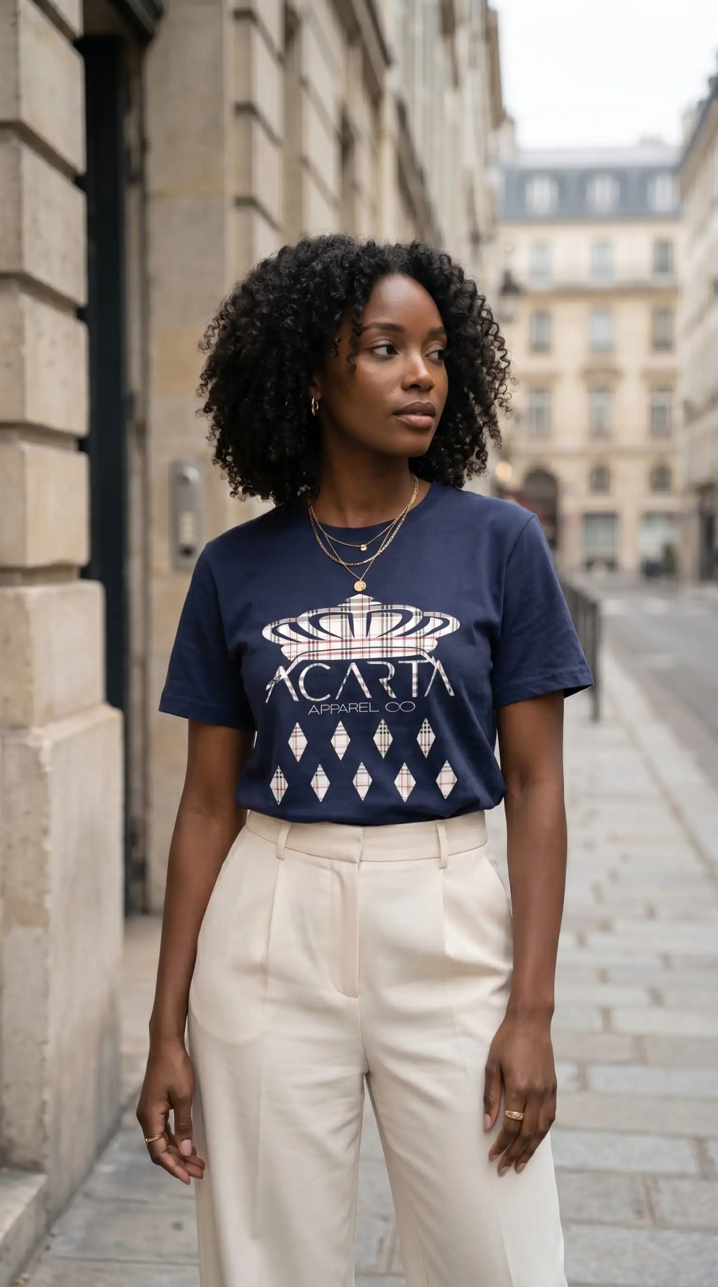 A woman with natural curly hair wearing a navy blue Too Dapper t-shirt with a crown graphic and beig.