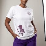 A woman modeling urban apparel from Too Dapper, wearing a white T-shirt with purple graphics and pur.