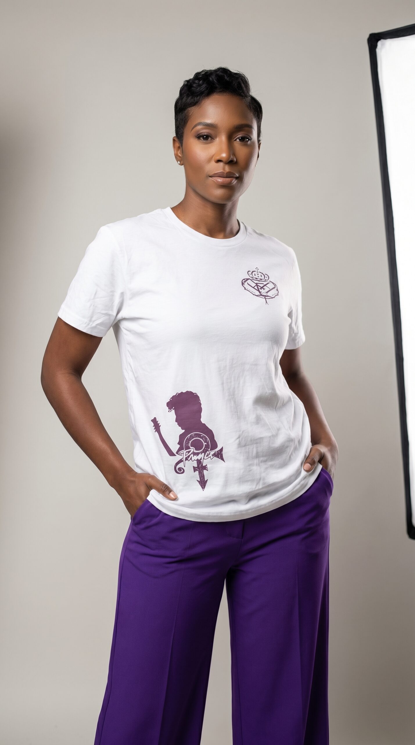 A woman modeling urban apparel from Too Dapper, wearing a white T-shirt with purple graphics and pur.